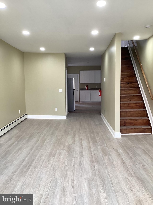 unfurnished living room featuring a baseboard heating unit and light hardwood / wood-style floors