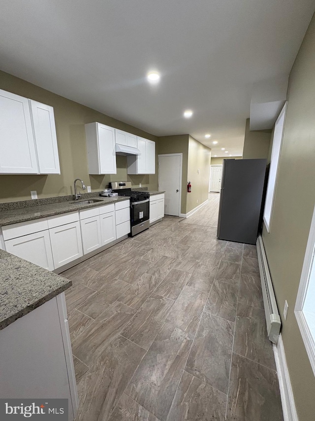 kitchen with sink, white cabinetry, dark stone counters, a baseboard radiator, and appliances with stainless steel finishes