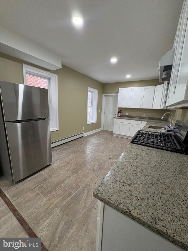 kitchen featuring sink, white cabinetry, a baseboard heating unit, light stone countertops, and stainless steel fridge