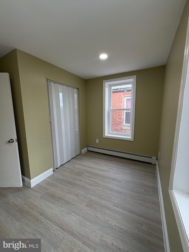 unfurnished bedroom featuring baseboard heating and light hardwood / wood-style flooring