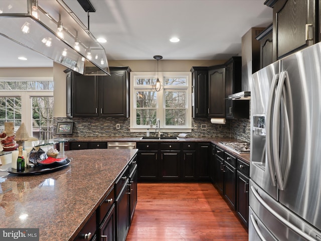 kitchen with appliances with stainless steel finishes, backsplash, dark stone counters, sink, and pendant lighting