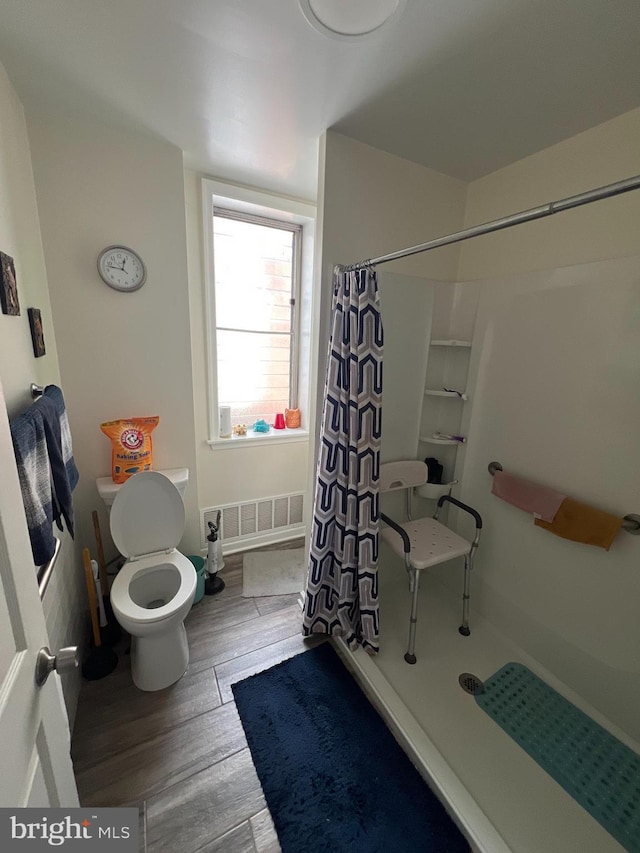 bathroom featuring wood-type flooring, toilet, and curtained shower