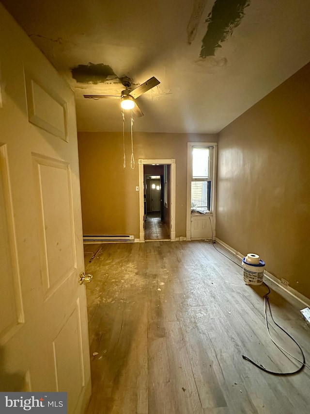 spare room featuring ceiling fan, wood-type flooring, and a baseboard heating unit