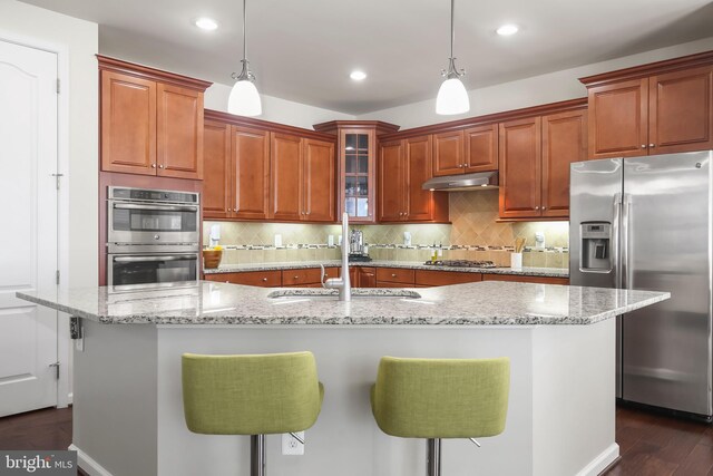 kitchen featuring hanging light fixtures, appliances with stainless steel finishes, a kitchen island with sink, and a kitchen breakfast bar