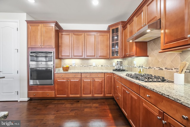 kitchen featuring decorative backsplash, light stone countertops, stainless steel appliances, and dark wood-type flooring