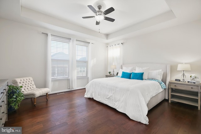 bedroom featuring ceiling fan, a raised ceiling, and dark wood-type flooring