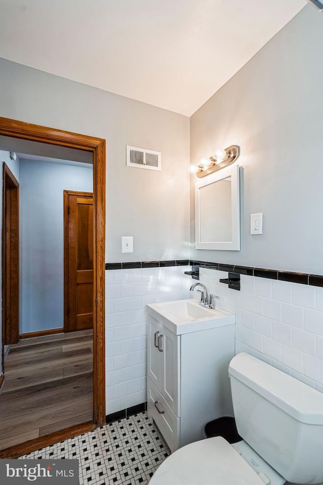 bathroom featuring tile patterned flooring, vanity, toilet, and tile walls