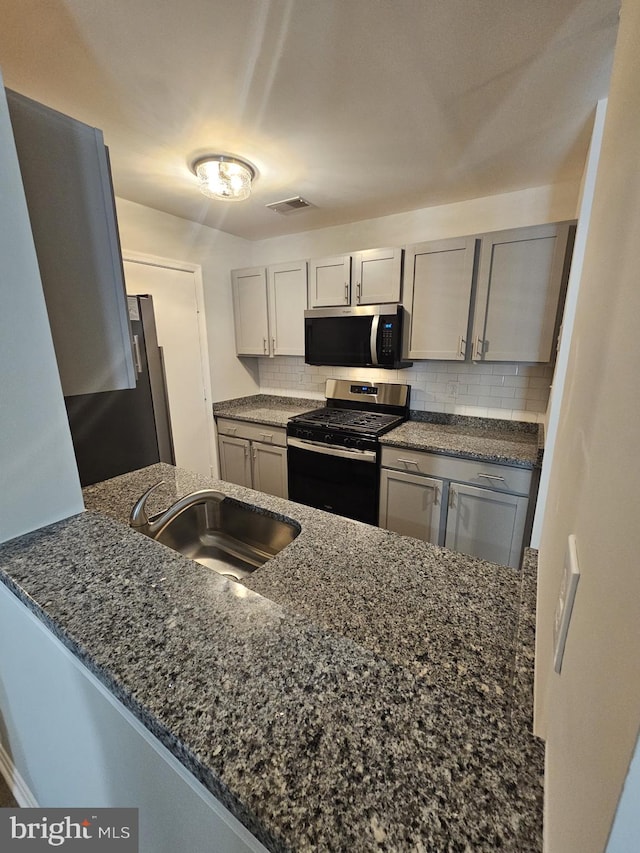 kitchen featuring sink, kitchen peninsula, dark stone counters, gray cabinetry, and appliances with stainless steel finishes