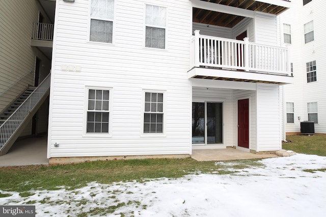 snow covered rear of property featuring a balcony, a patio area, and central AC unit