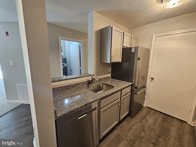 kitchen featuring dishwasher, dark stone counters, dark wood-type flooring, refrigerator, and sink