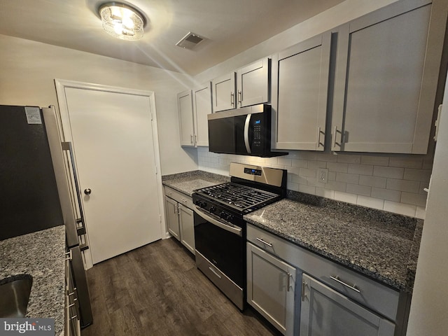 kitchen with decorative backsplash, dark hardwood / wood-style flooring, gray cabinetry, appliances with stainless steel finishes, and dark stone countertops