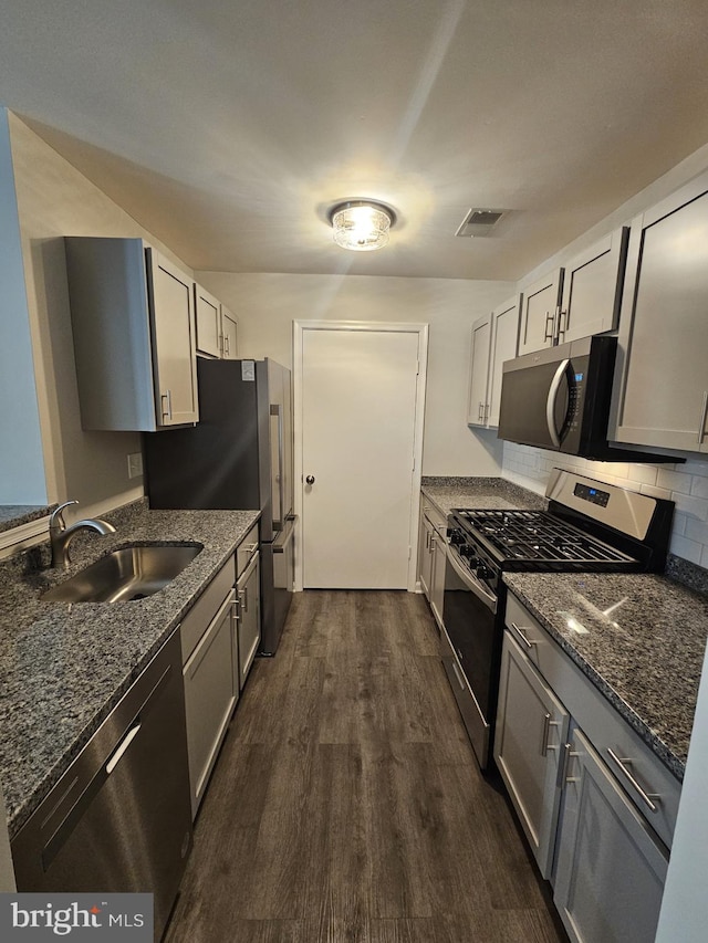 kitchen featuring stainless steel appliances, dark stone counters, dark hardwood / wood-style flooring, and sink