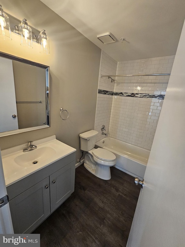 full bathroom with hardwood / wood-style floors, tiled shower / bath combo, vanity, and toilet