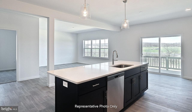 kitchen with stainless steel dishwasher, sink, light hardwood / wood-style floors, hanging light fixtures, and an island with sink