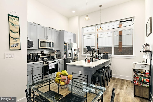 kitchen with a breakfast bar area, gray cabinets, stainless steel appliances, and decorative light fixtures