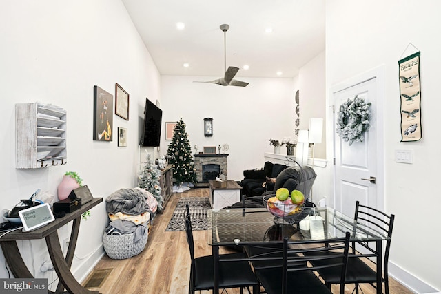 dining room with hardwood / wood-style flooring, ceiling fan, and a stone fireplace