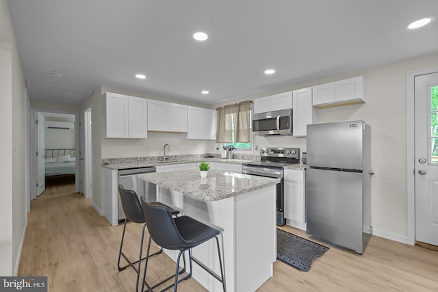 kitchen featuring white cabinetry, a center island, stainless steel appliances, and light wood-type flooring