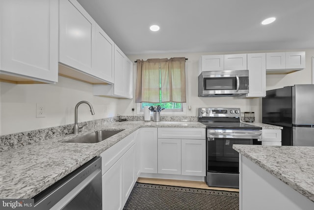 kitchen featuring white cabinets, stainless steel appliances, light stone counters, and sink