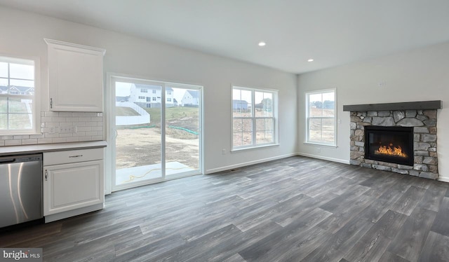 unfurnished living room featuring a stone fireplace, dark hardwood / wood-style flooring, and a healthy amount of sunlight