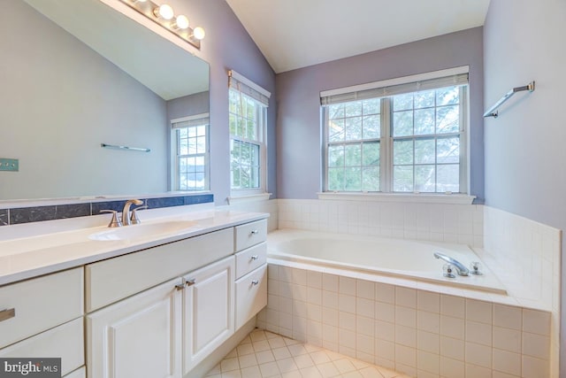 bathroom with tile patterned flooring, vanity, lofted ceiling, and tiled tub