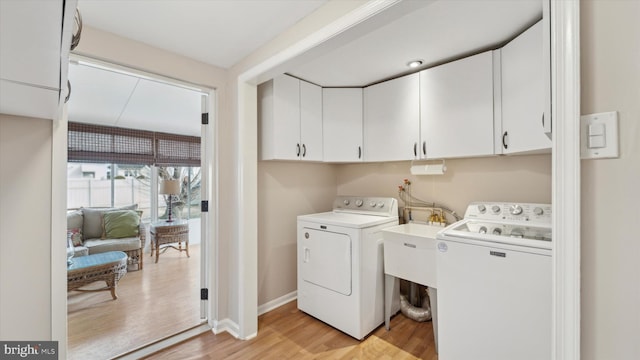 laundry area featuring washer and clothes dryer, light hardwood / wood-style floors, and cabinets