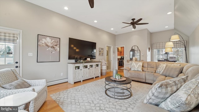 living room with lofted ceiling, light wood-type flooring, a baseboard radiator, and a healthy amount of sunlight