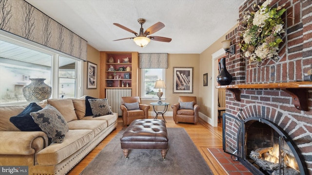 living room featuring ceiling fan, a brick fireplace, built in features, a textured ceiling, and hardwood / wood-style flooring