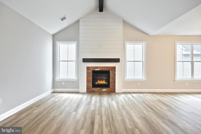 unfurnished living room featuring lofted ceiling with beams, a healthy amount of sunlight, light hardwood / wood-style floors, and a fireplace