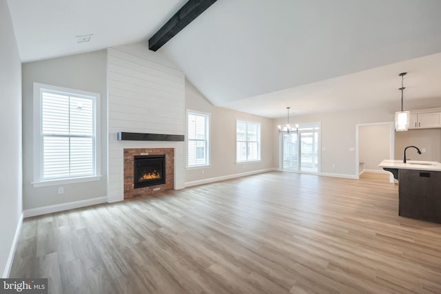 unfurnished living room featuring vaulted ceiling with beams, sink, an inviting chandelier, and light wood-type flooring