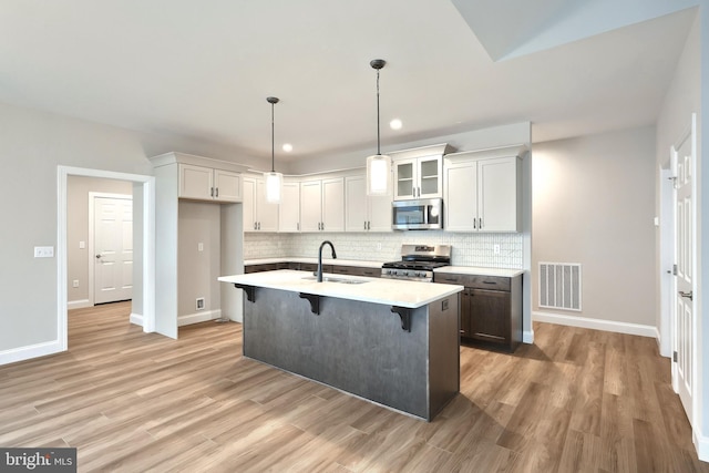 kitchen with sink, an island with sink, appliances with stainless steel finishes, decorative light fixtures, and a breakfast bar area