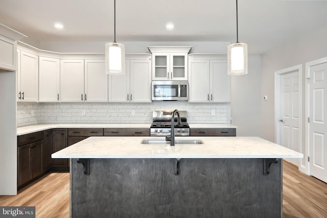 kitchen with appliances with stainless steel finishes, light stone counters, a kitchen island with sink, pendant lighting, and white cabinetry