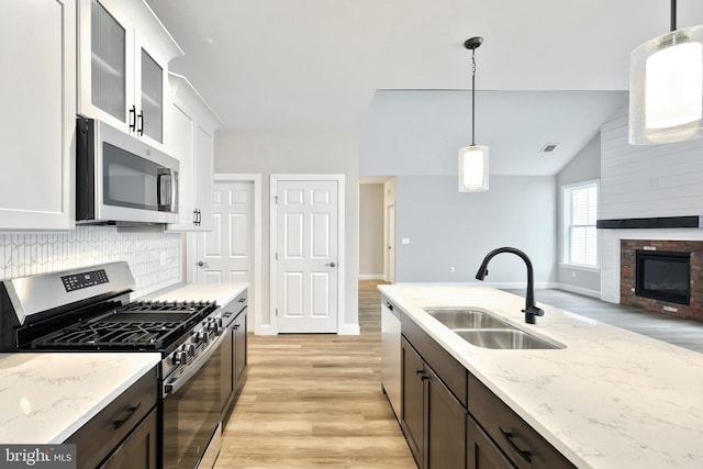 kitchen with dark brown cabinets, stainless steel appliances, vaulted ceiling, sink, and white cabinets