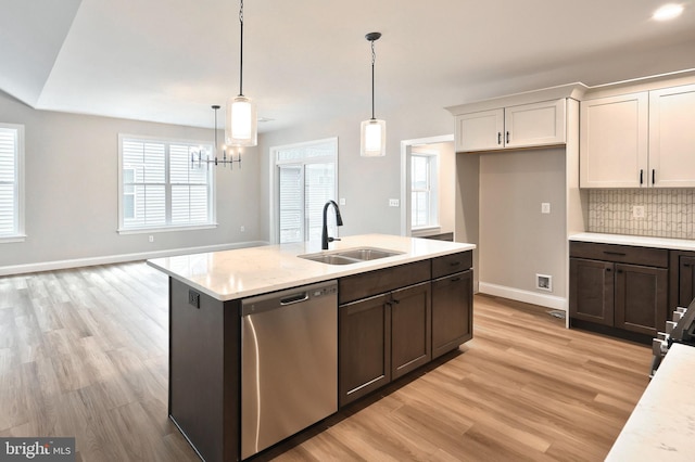 kitchen with light stone counters, stainless steel dishwasher, sink, white cabinets, and hanging light fixtures