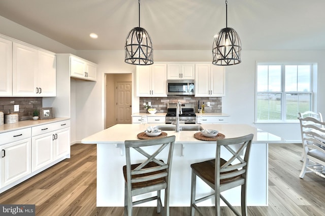 kitchen with appliances with stainless steel finishes, backsplash, a kitchen island with sink, sink, and white cabinets