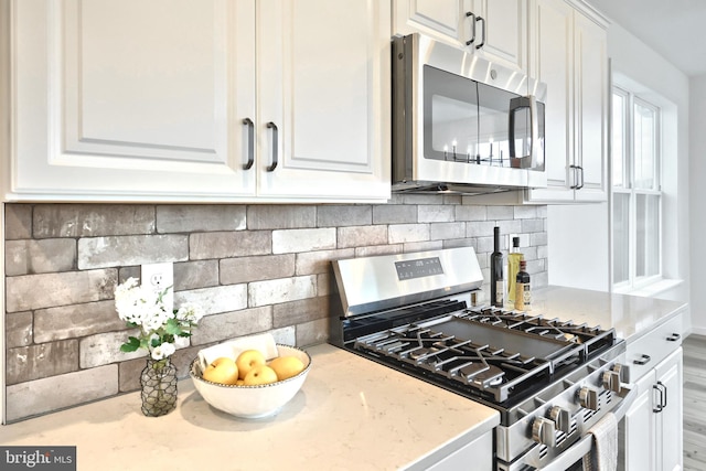 kitchen featuring appliances with stainless steel finishes, backsplash, white cabinetry, and light stone counters