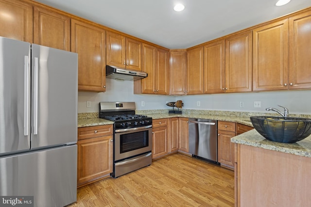 kitchen featuring light stone counters, sink, appliances with stainless steel finishes, and light wood-type flooring