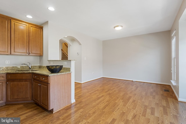 kitchen with light stone counters, sink, kitchen peninsula, and light wood-type flooring