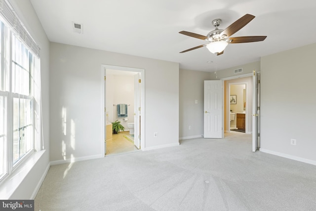 unfurnished bedroom featuring ceiling fan, multiple windows, ensuite bathroom, and light carpet