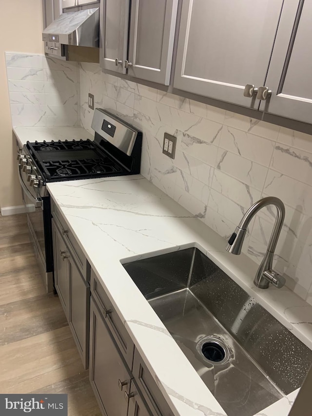 kitchen featuring gas range, light stone countertops, sink, tasteful backsplash, and extractor fan