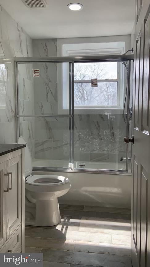 full bathroom with vanity, enclosed tub / shower combo, and toilet