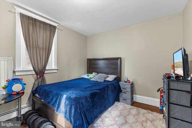 bedroom featuring hardwood / wood-style flooring and a baseboard heating unit