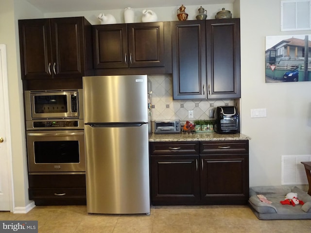 kitchen featuring light tile patterned floors, appliances with stainless steel finishes, tasteful backsplash, light stone counters, and dark brown cabinetry