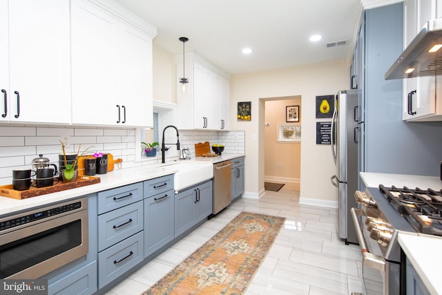 kitchen featuring white cabinetry, decorative light fixtures, appliances with stainless steel finishes, wall chimney range hood, and backsplash