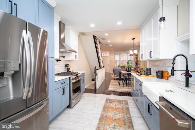 kitchen with wall chimney exhaust hood, appliances with stainless steel finishes, decorative light fixtures, and white cabinets