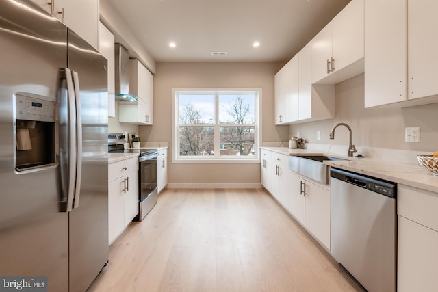 kitchen with wall chimney exhaust hood, sink, white cabinets, and appliances with stainless steel finishes