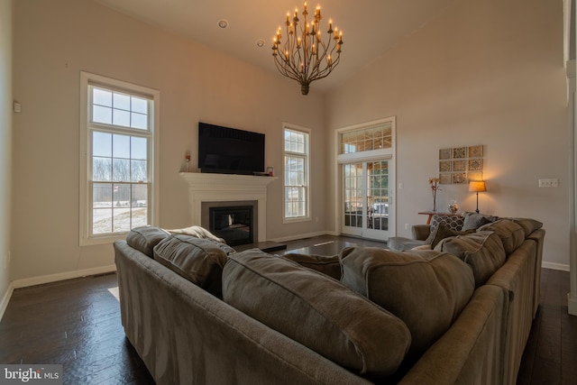 living room with a notable chandelier, dark wood-type flooring, plenty of natural light, and high vaulted ceiling