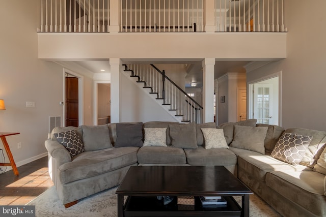 living room featuring crown molding, a towering ceiling, light hardwood / wood-style flooring, and ornate columns