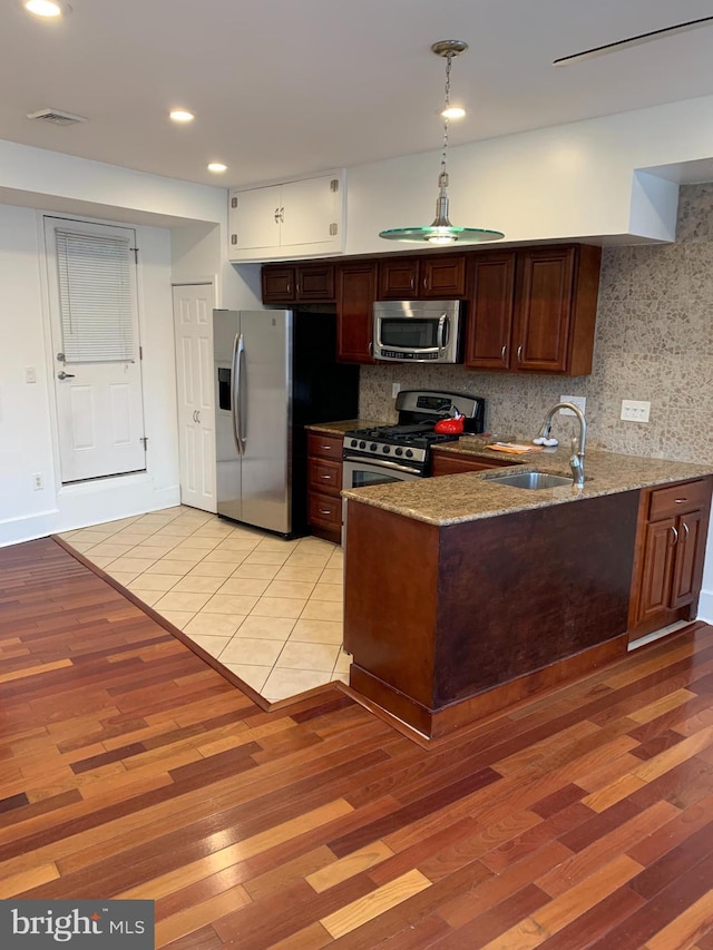 kitchen featuring light stone countertops, appliances with stainless steel finishes, light hardwood / wood-style floors, and sink