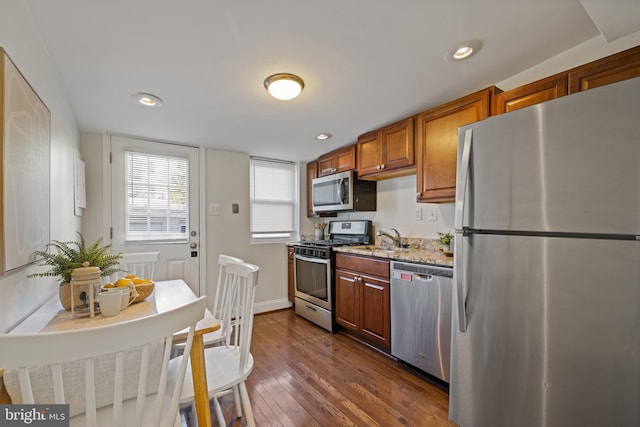 kitchen featuring dark wood-type flooring, stainless steel appliances, light stone countertops, and sink