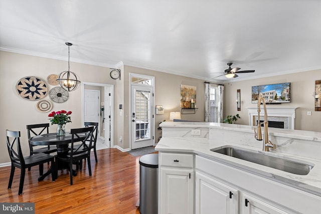 kitchen with white cabinetry, sink, ceiling fan, decorative light fixtures, and light wood-type flooring